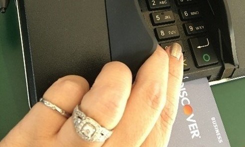 Caucasian woman with engagement ring using pin pad to complete credit card transaction